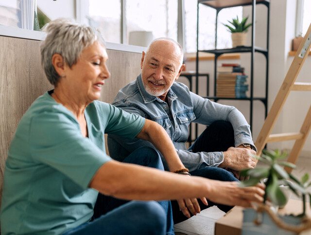 Senior couple sitting on a floor while renovating house, cardboard boxes are around them