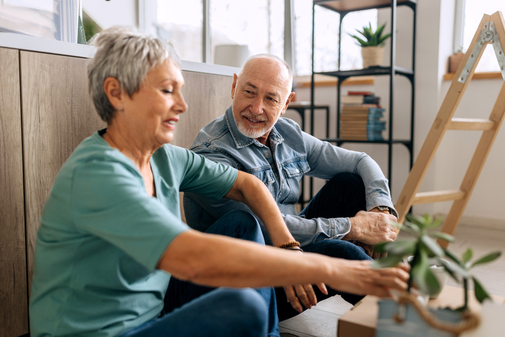 Senior couple sitting on a floor while renovating house, cardboard boxes are around them