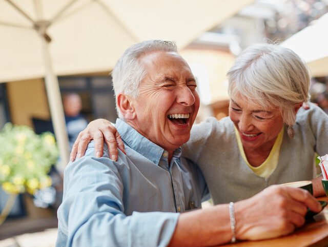 man and woman sitting outside laughing while they enjoy a meal